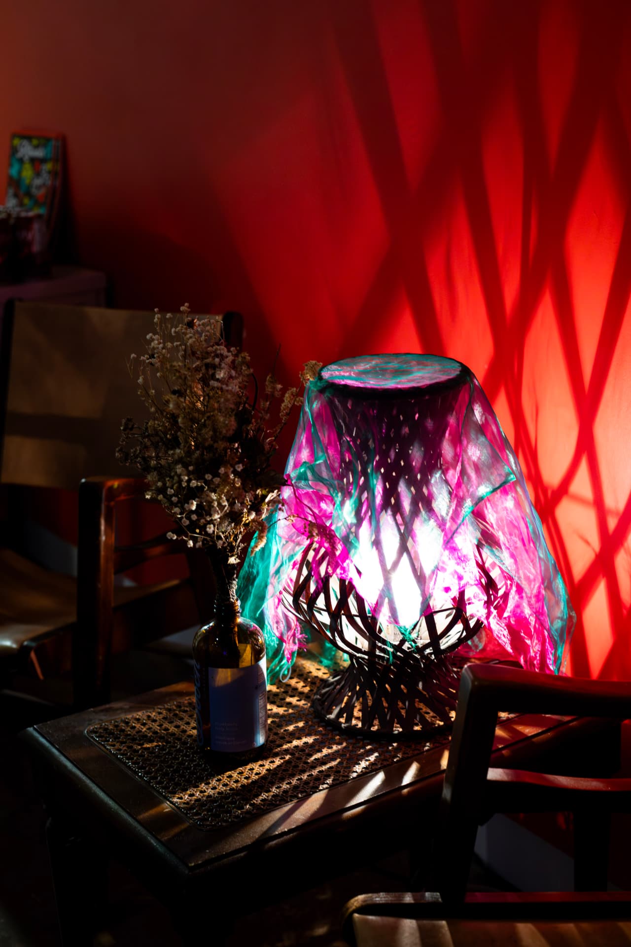A veiled lamp glowing pink and teal against a warm red wall